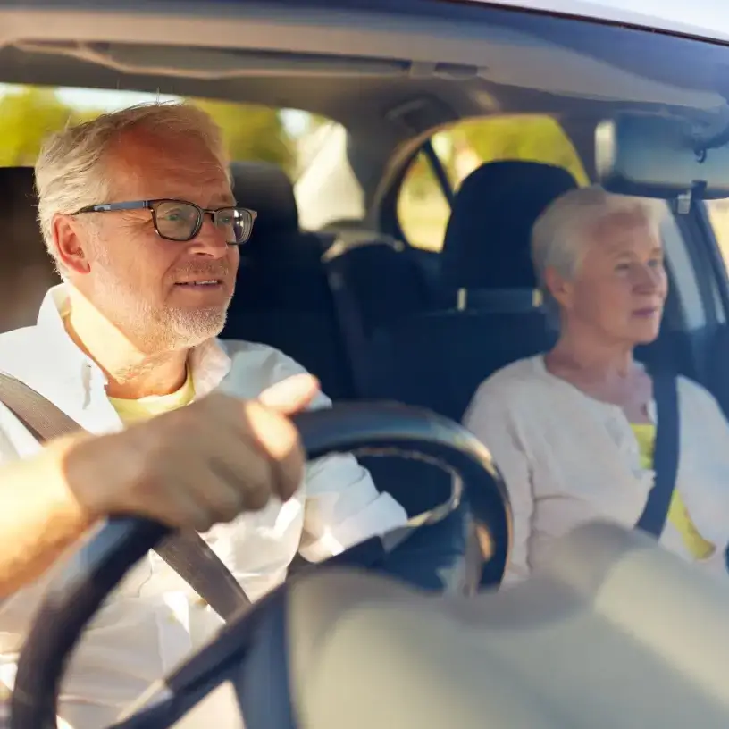 A male pensioner driving a car with a senior female in the passenger seat.