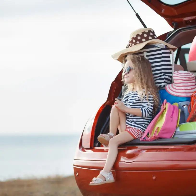 Child sitting in the back of car surrounded by holiday bags