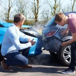 Two men looking at their collided cars after an accident.