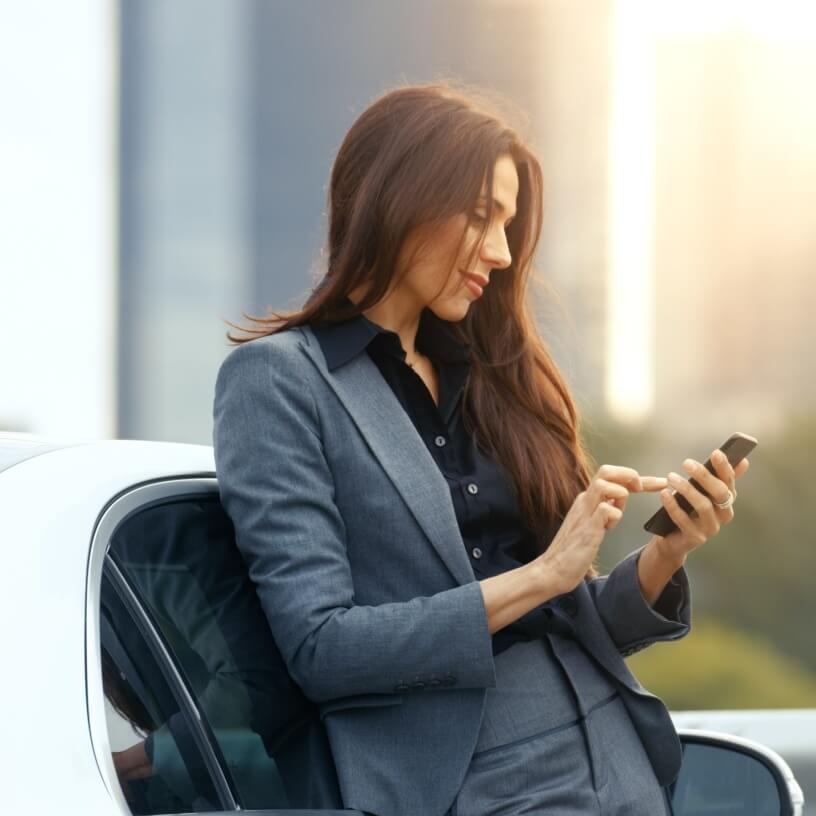 A business woman texting on a phone next to her car.