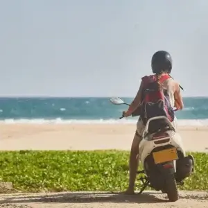 Woman tourist sitting on a moped overlooking the beach