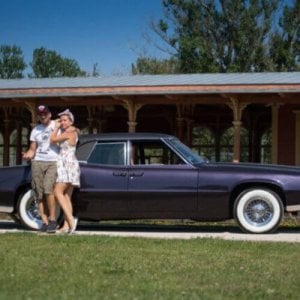 A man and a woman standing next to a purple classic car.