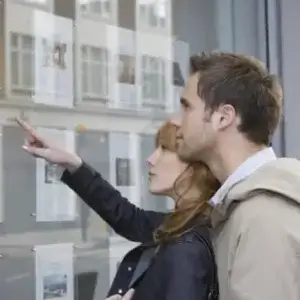 A couple looking for a new home in a real estate agent's window.