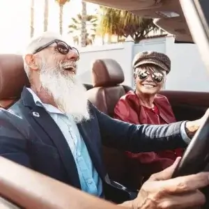 A happy senior couple riding in a convertible car.