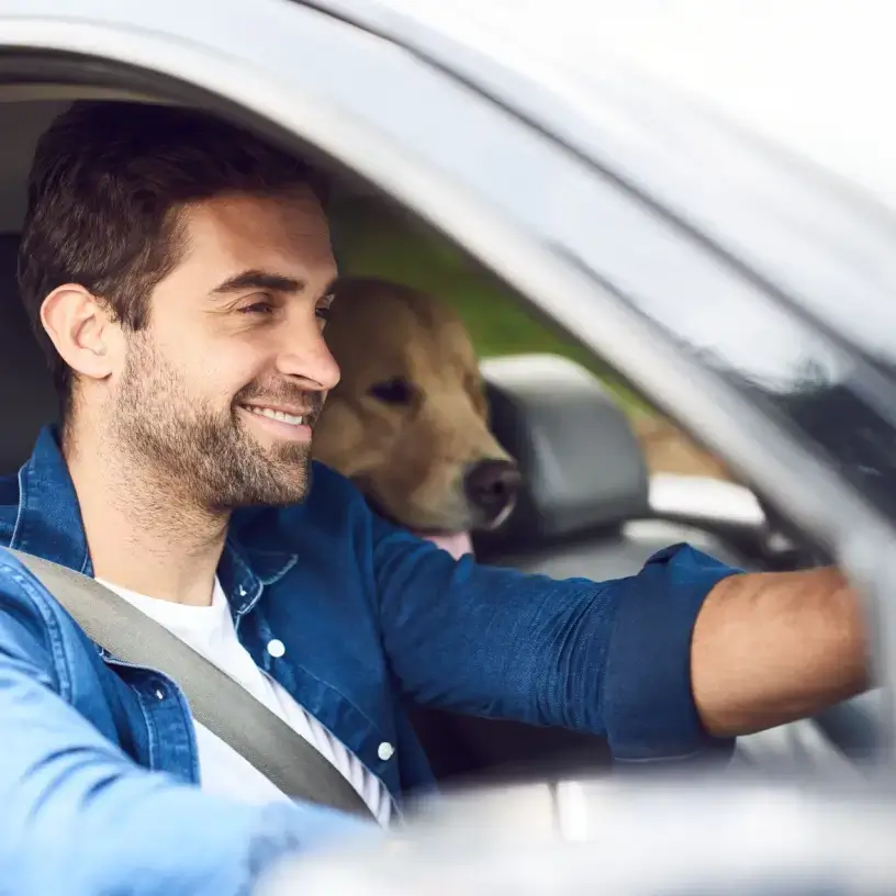 A man driving a car with a dog in the back seat.