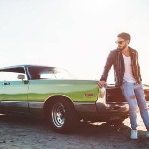 A man standing next to the hood of his green classic car.