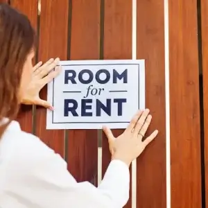 A woman hanging up a "room for rent" sign.