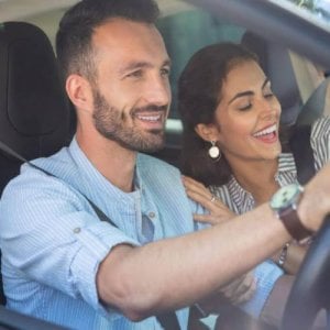 Man in a striped shirt driving with a woman in the passenger seat.