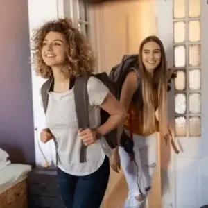 Two young female travellers walking into a backpackers hostel.