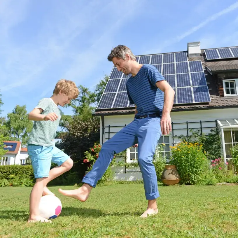 Father and son playing on lawn in front of house with solar panels