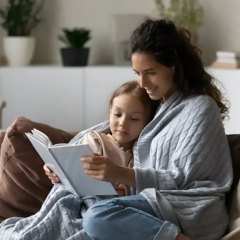 Mother and child on couch reading book with blankets