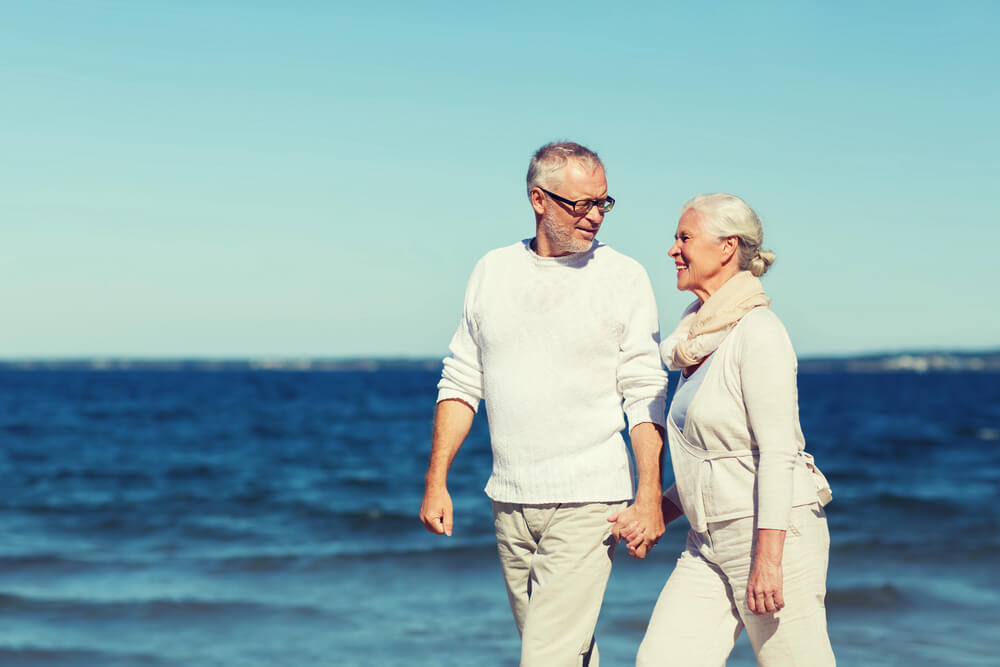 happy senior couple holding hands and walking on summer beach