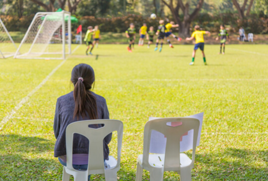 mother-sitting-on-the-field-sideline-watching-children-play-sport