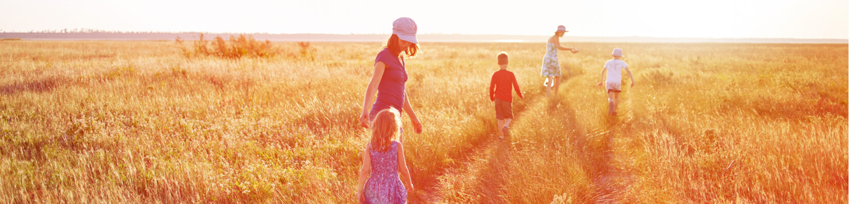 Two adults and three children walking in grasslands at sunset
