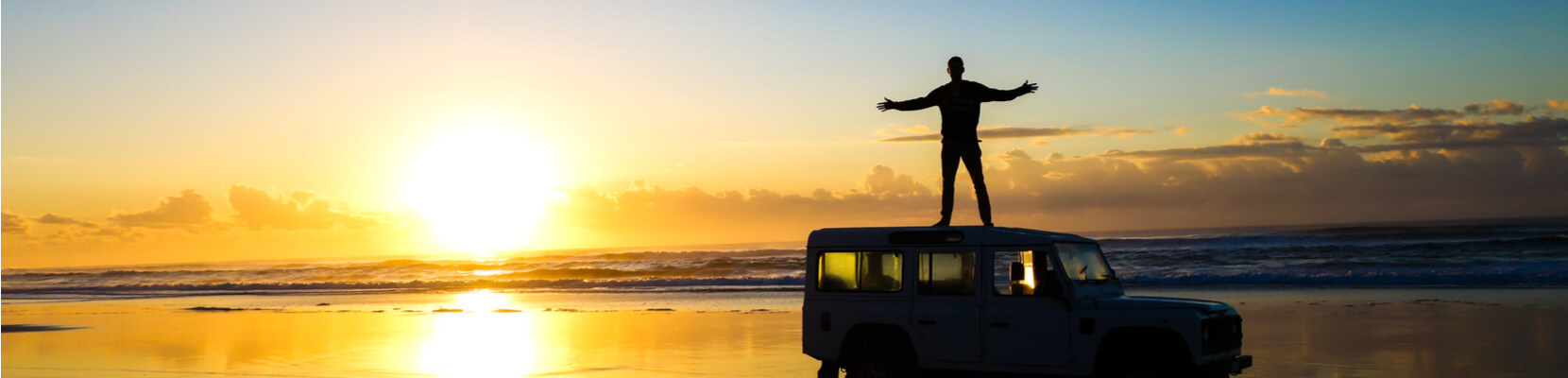 man standing on jeep at beach during sunrise