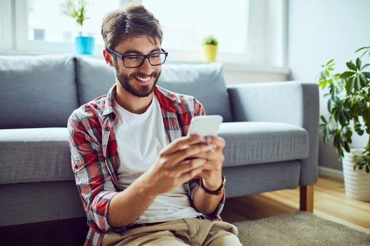 man using a mobile phone sitting against the couch