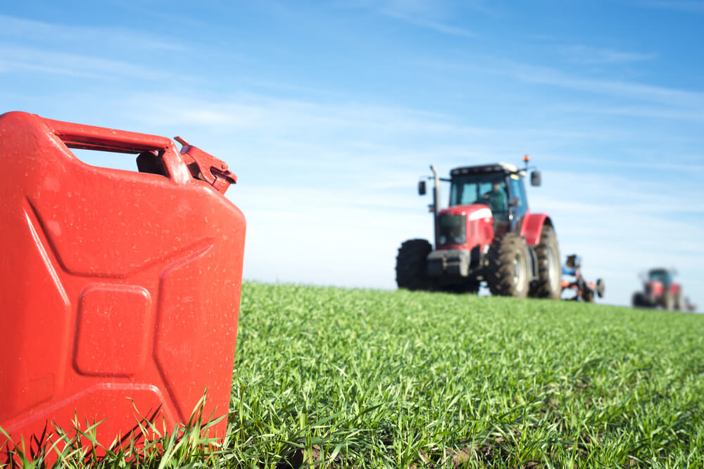 A red gasoline can on a field with two red tractors producing ethanol fuel