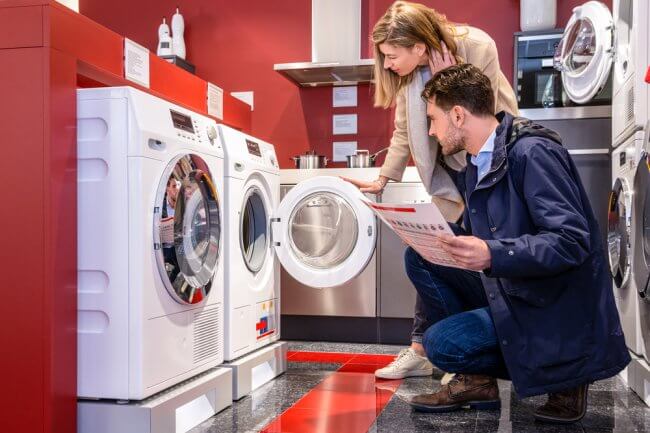 A young couple looking at a washing machine in a shop