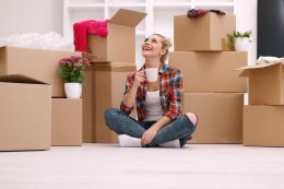 a woman drinking coffee while sitting next to cardboard boxes