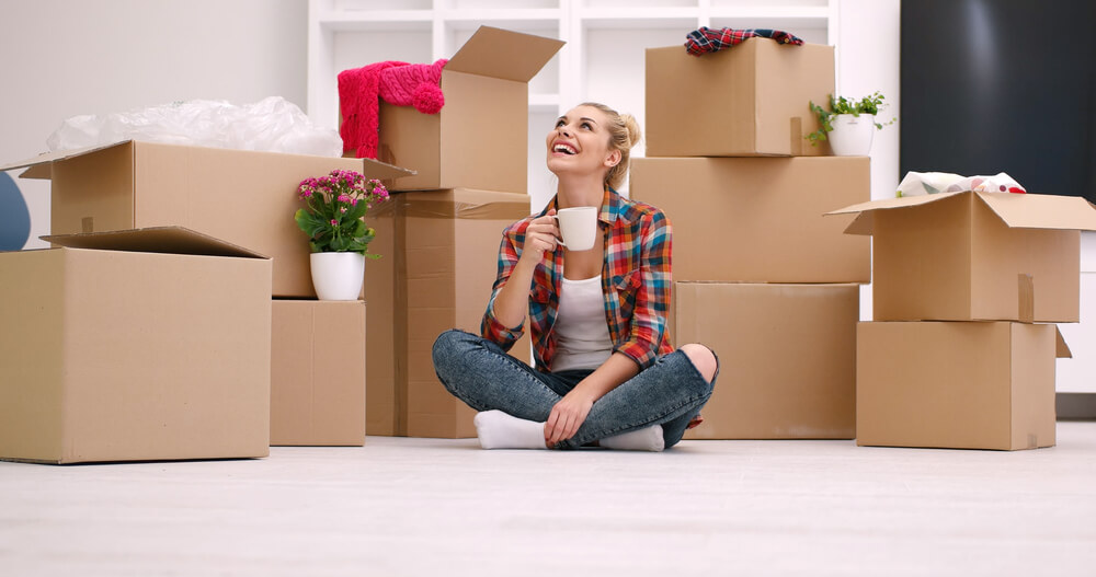 a woman drinking coffee while sitting next to cardboard boxes