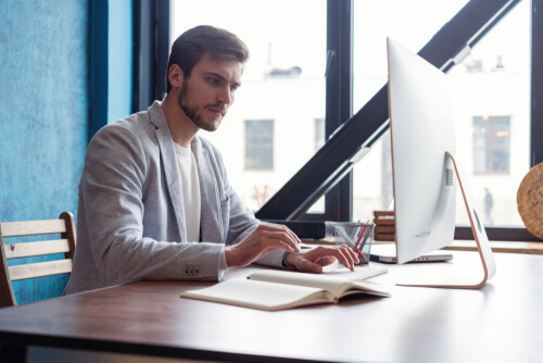 a man using a computer at a desk next to a window