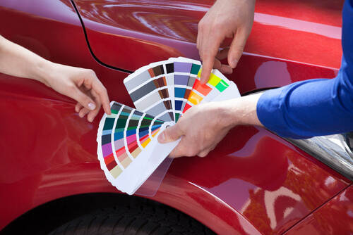 a man holds a colour chart against a red car
