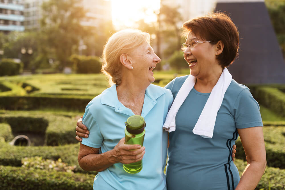 two older women dressed in workout clothes and smiling while exercising outdoors