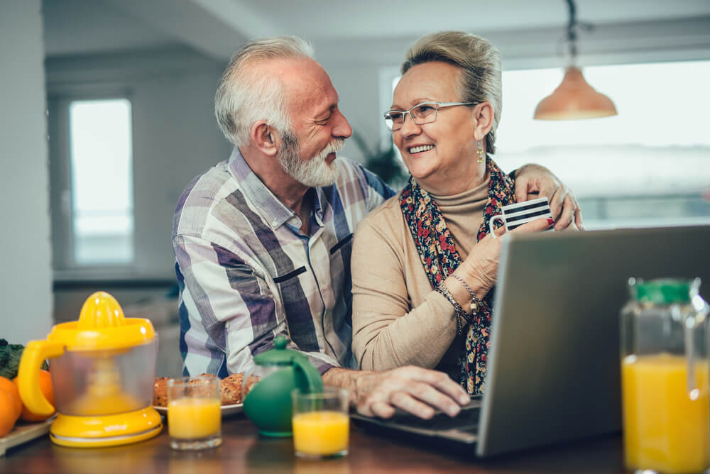 an older couple using a laptop on the kitchen bench