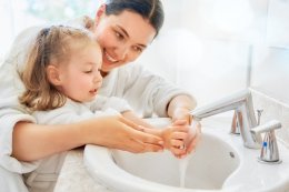 Mother helping her daughter wash her hands with bar soap in the sink