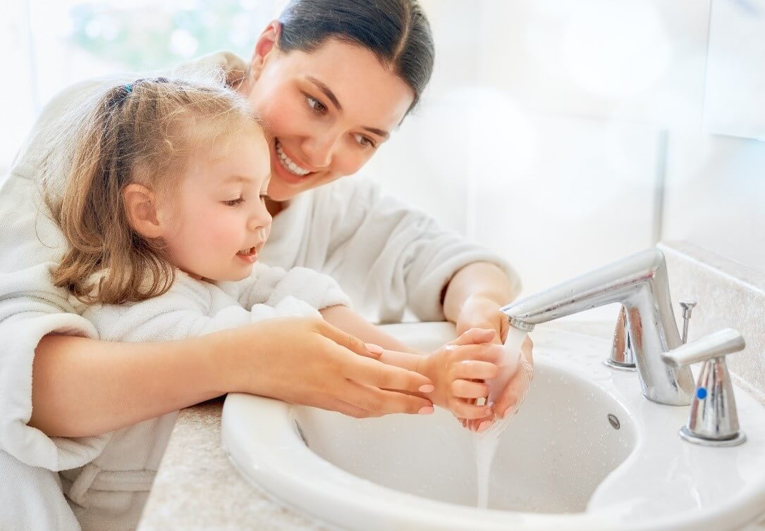 Mother helping her daughter wash her hands with bar soap in the sink