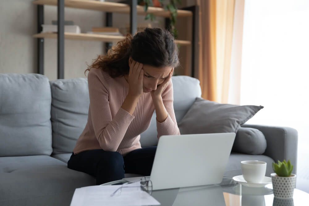 a woman managing her finances at home using a laptop holding head in hands