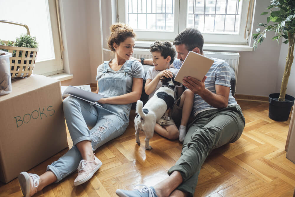 A family of three sitting on the floor of their new home with a dog