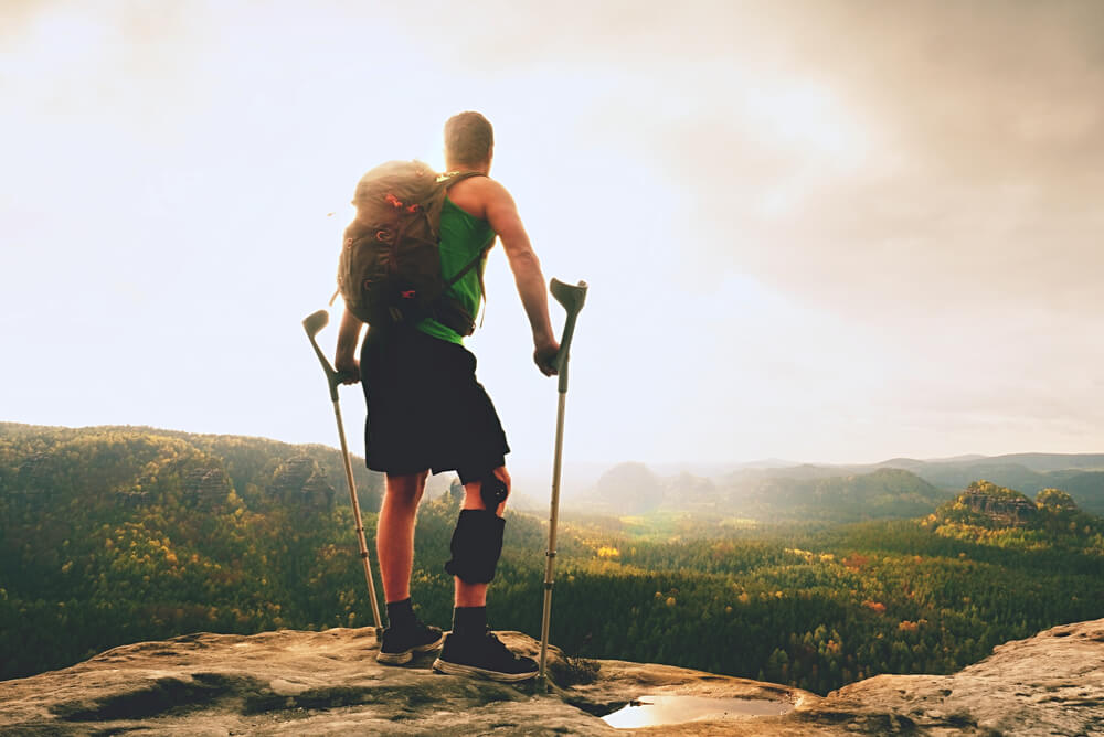 Man with an injured leg hiking to the top of a mountain