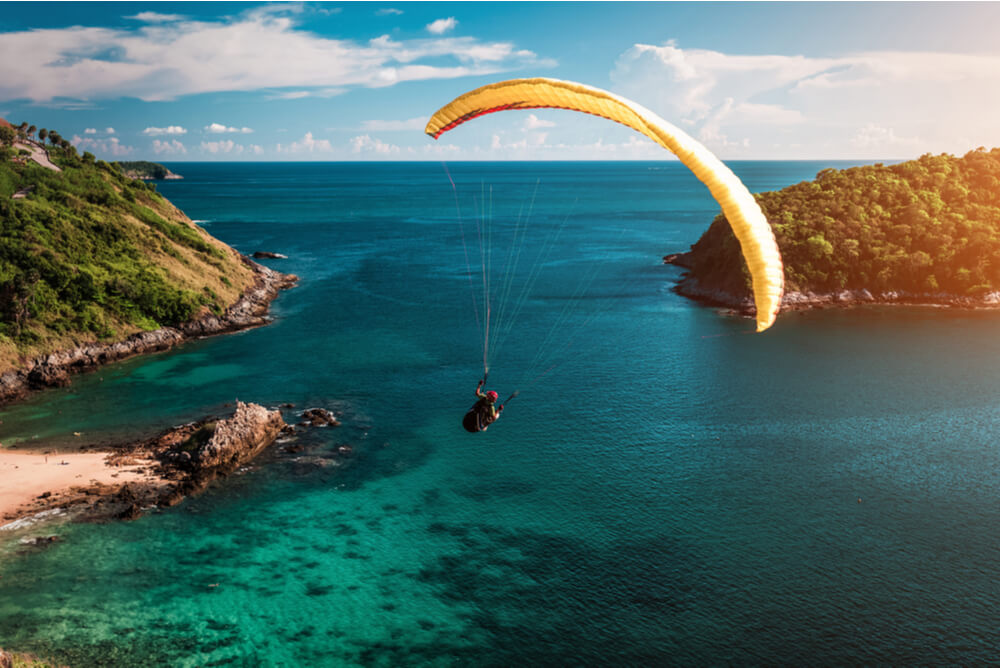 paraglider flying over water at sunset