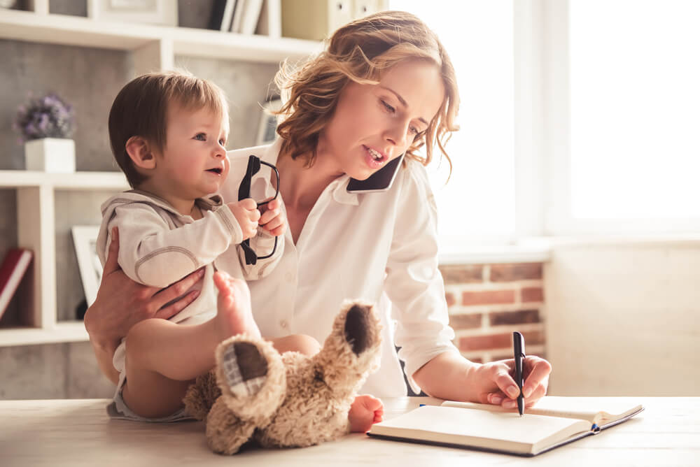 mum holding baby while talking on phone and working from home