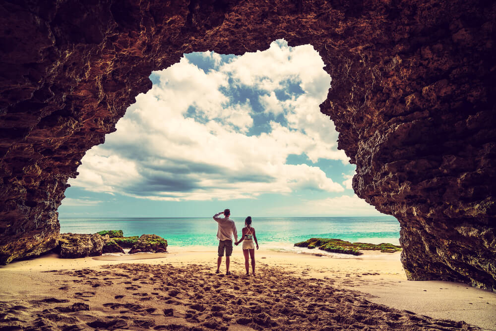 a couple standing in a cave at the beach