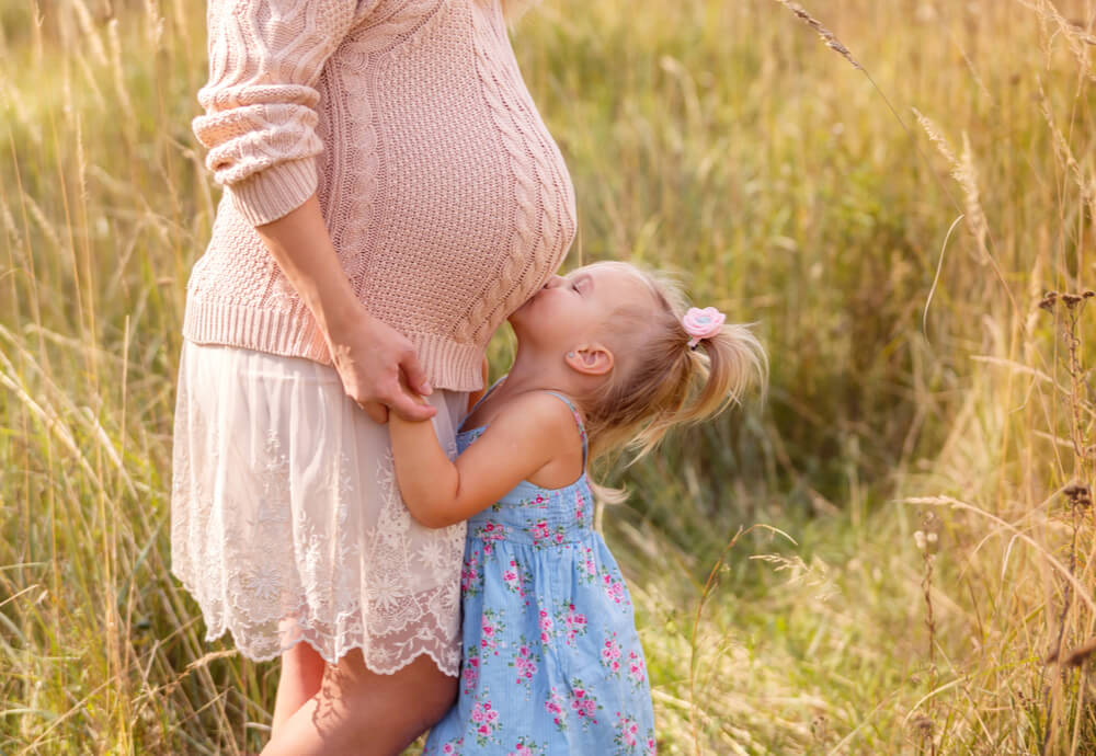 a little girl kissing her mother's pregnant belly