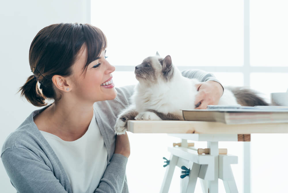 A woman kneeling down close to her cat.