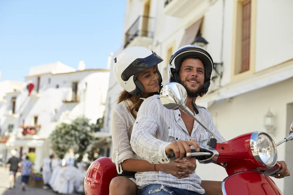 a couple riding on a scooter together through the streets of BIiza, Spain