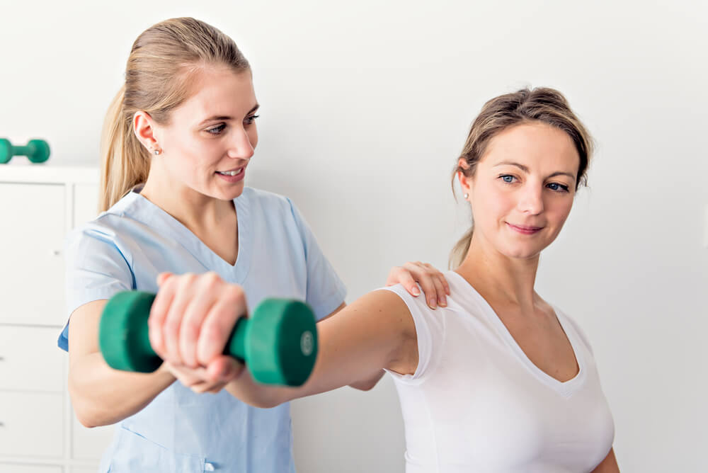 a physiotherapist helps a female patient lift a weight