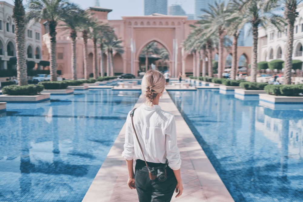 a blonde woman in Dubai facing a walkway between pools