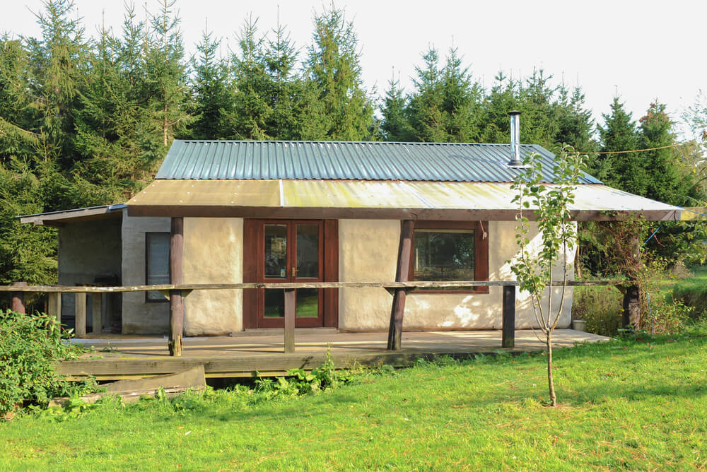 a straw bale house with corrugated roof and wooden patio