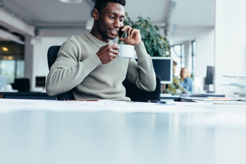 an office working drinking a coffee and talking on the phone while at his desk