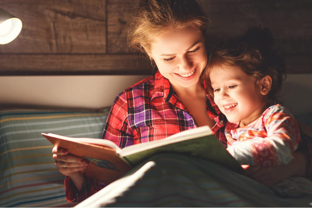 a mother reading her daughter a story by lamplight