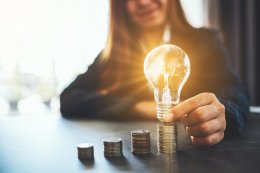 a woman holding a lightbulb on pillars of coins