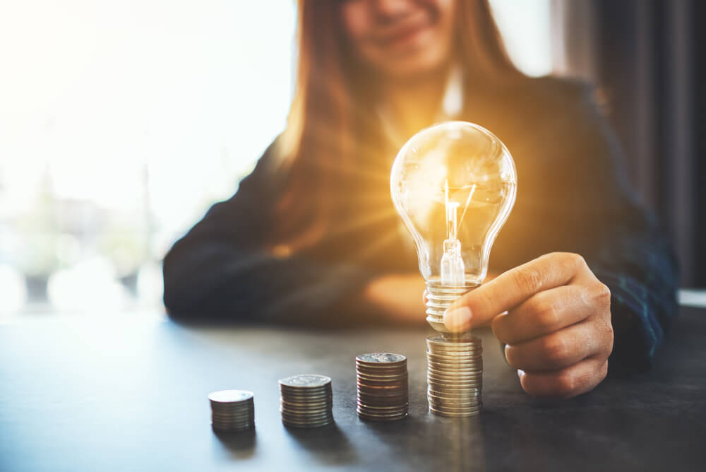 a woman holding a lightbulb on pillars of coins
