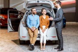 a car salesman talks to a couple sitting in the boot of an electric car