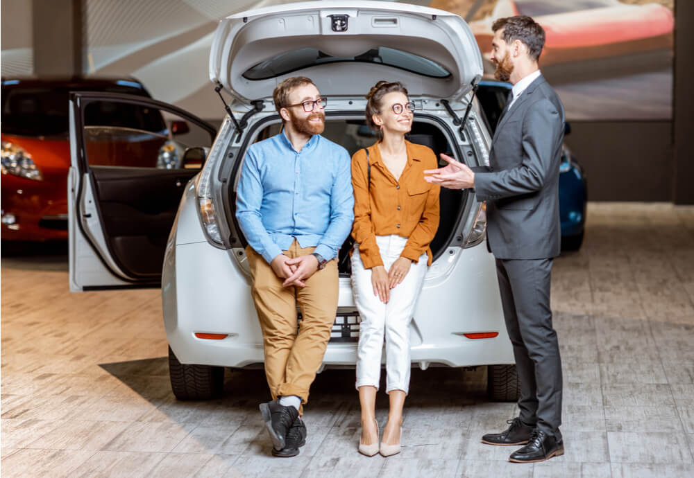 a car salesman talks to a couple sitting in the boot of an electric car