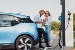 a couple standing next to their blue EV while it recharges