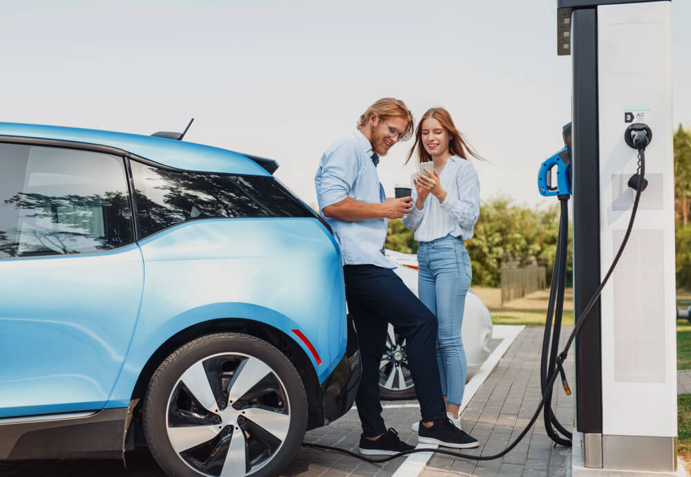 a couple standing next to their blue EV while it recharges